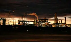 The outline of a factory at dusk with smoke coming out of it.