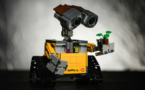 A black and yellow toy robot holding a toy plant. Written on the robot are the words wall-E.