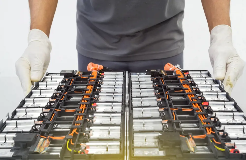 A technician carries a tray of lithium ion batteries, connected with orange cabling.
