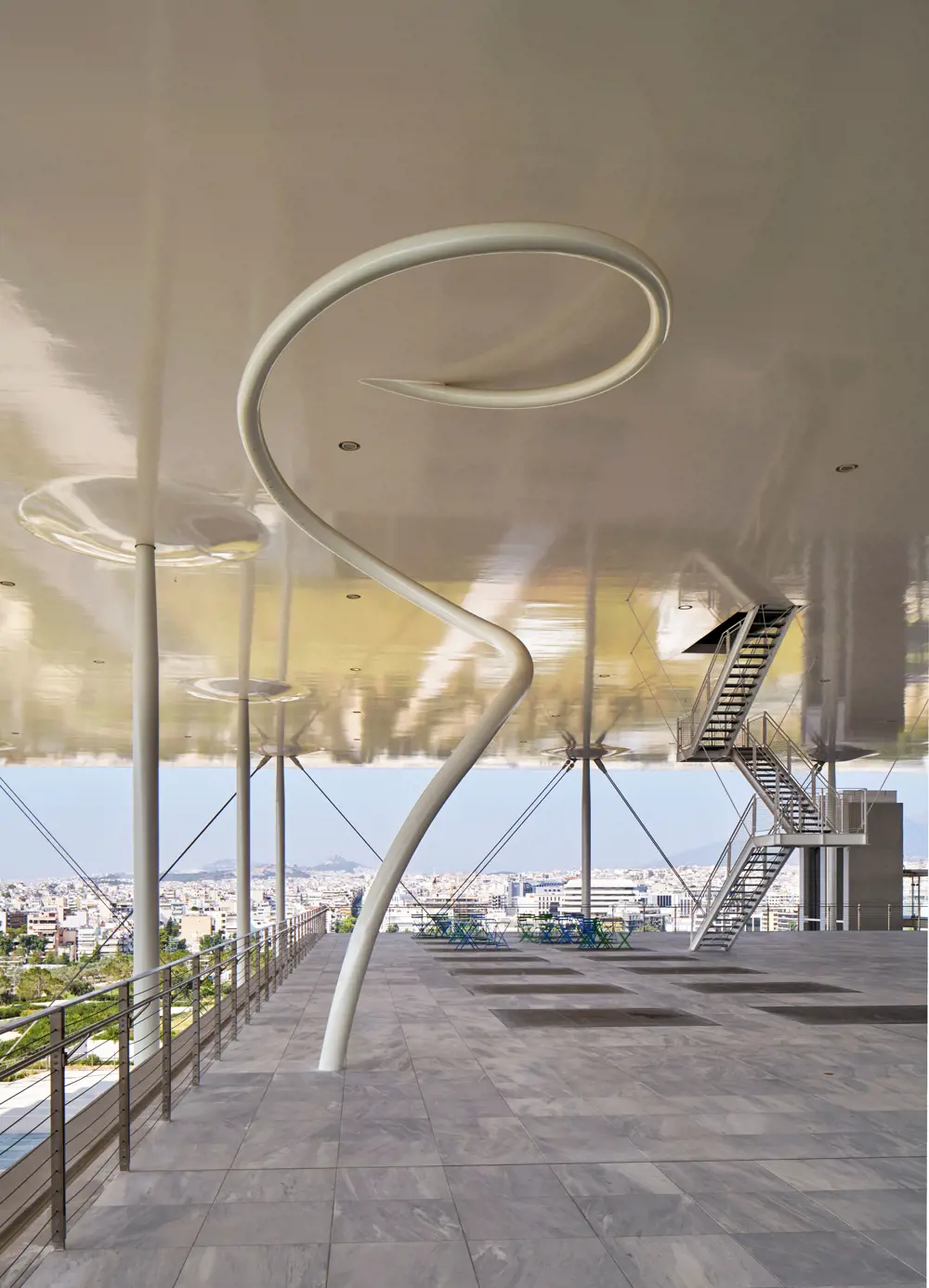 A white thin spiral structure going down from a ceiling to a floor.