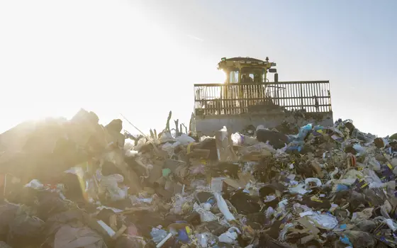 A tractor on top of a pile of rubbish at a landfill site.