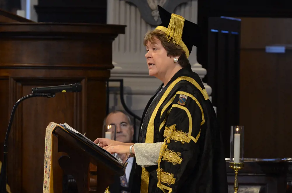Baroness Brown in academic robes, speaking at at a podium inside a cathedral.