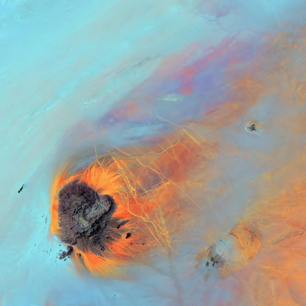 A satellite image of northwestern Sudan in the Sahara desert. The desert appears blue, truck tracks appear orange, and a granite dome appears grey.