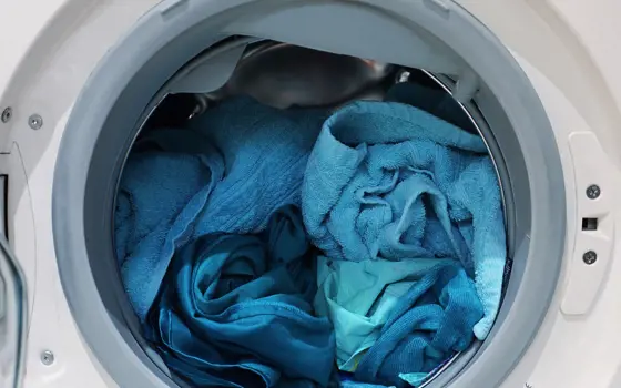 An open washing machine appliance, containing a mixture of different blue fabrics.