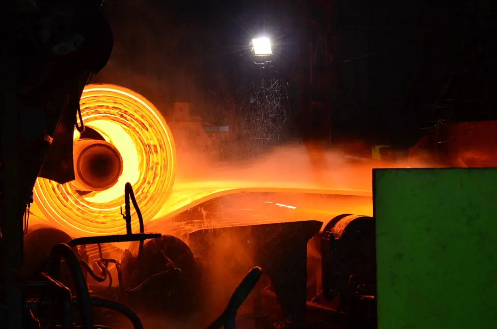 A glowing orange roll of heated, flattened steel in a steel mill
