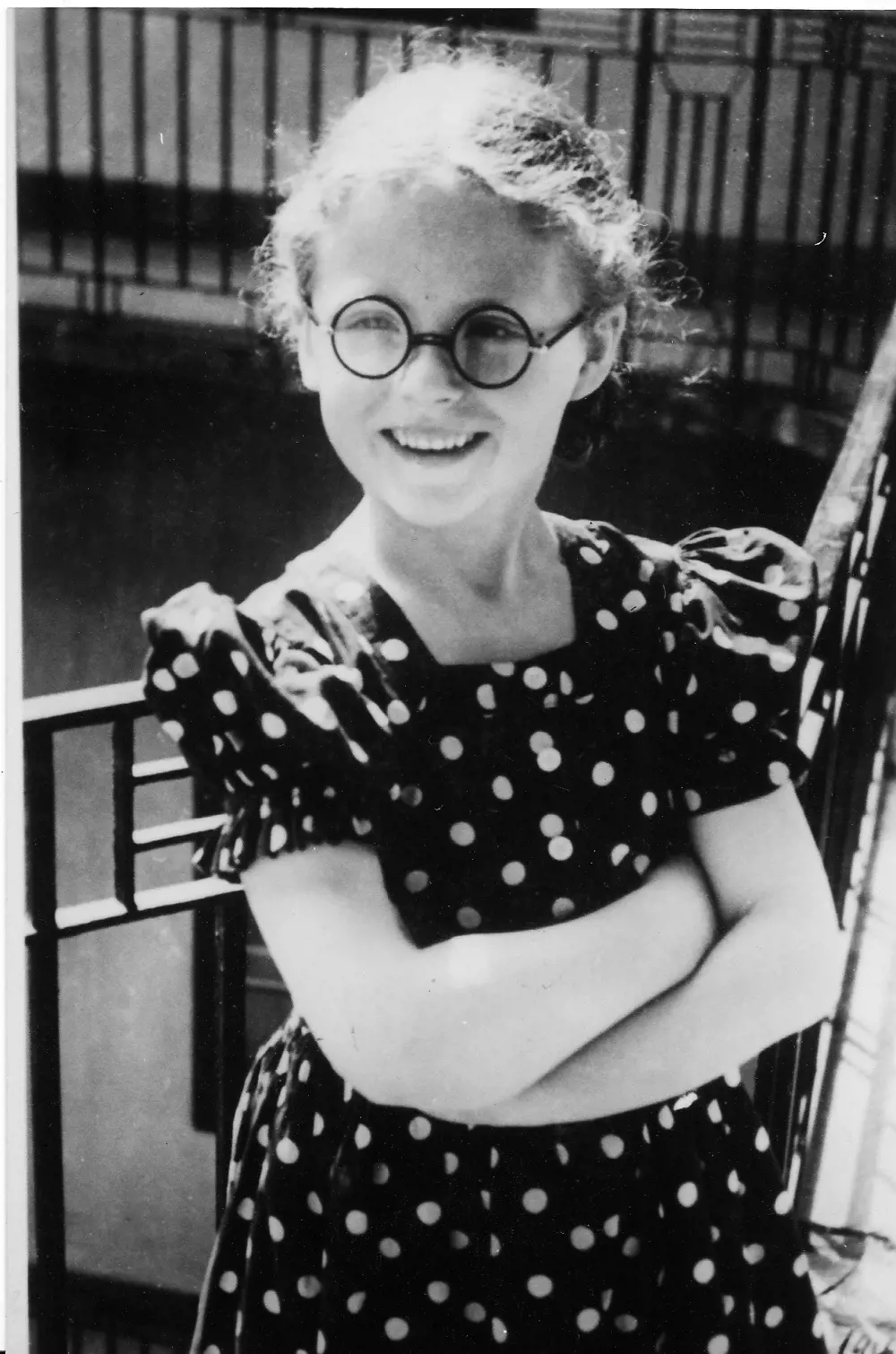 A black and white photograph of a six-year-old girl wearing glasses and a polka dot dress.