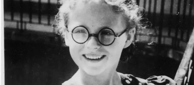 A black and white photograph of a six-year-old girl wearing glasses and a polka dot dress.