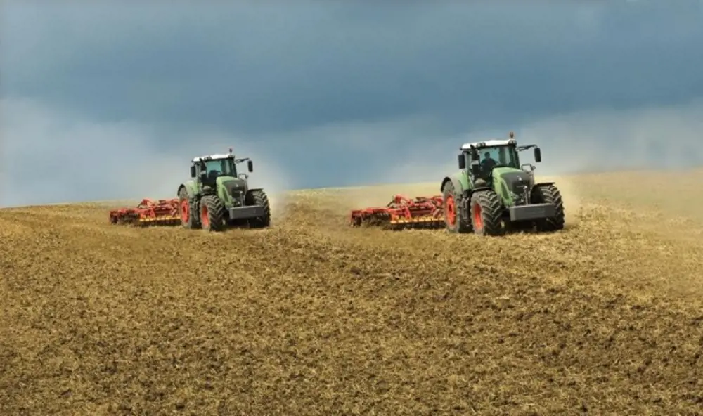 A tractor being driven in a field with another tractor following behind. 