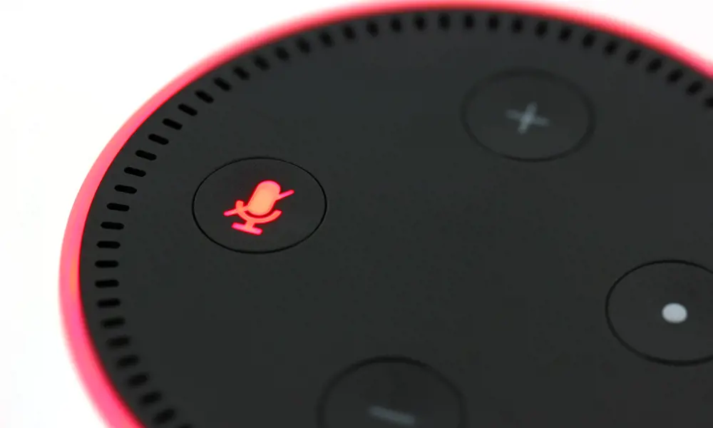 The Amazon Echo dot. The edge of the device and the microphone symbol on the device are lit up in a red colour.