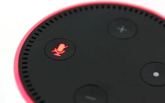 The Amazon Echo dot. The edge of the device and the microphone symbol on the device are lit up in a red colour.
