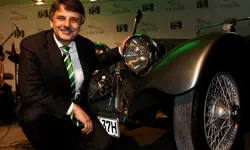 Ralf Speth, crouching next to an old Jaguar at a formal event in Germany.