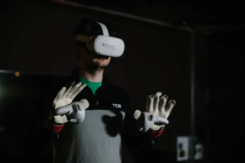 A man wearing a virtual reality headset and handheld controllers on top of his goalie gloves.