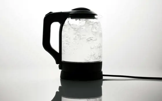 A transparent electric kettle boiling water which is bubbling inside. 