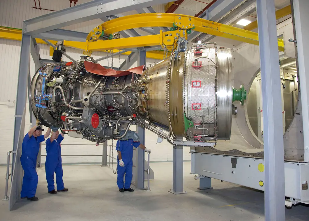 A Rolls-Royce MT30 gas turbine in a factory with three people underneath.