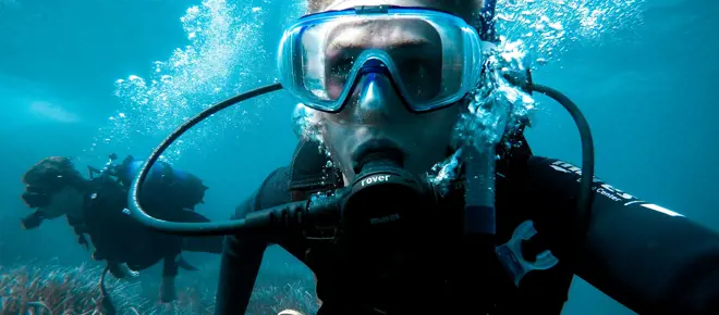 Close up of a man underwater, breathing through scuba gear.