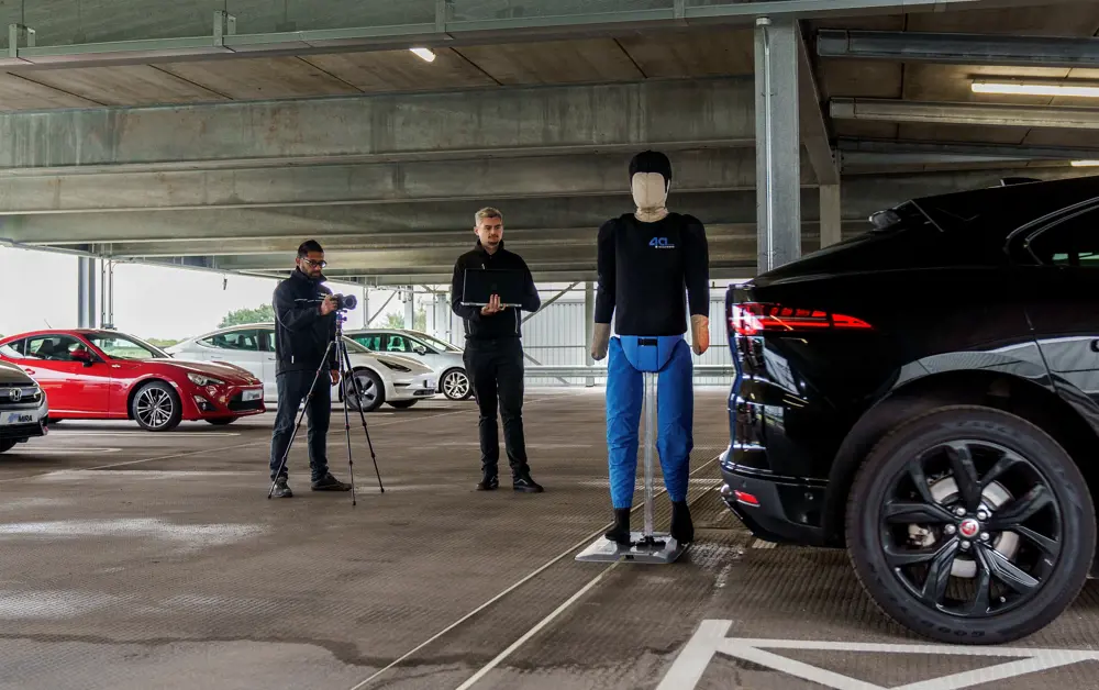 Two male engineers taking notes testing whether an autonomous car will reverse out of a spot, with a dummy obstructing it.