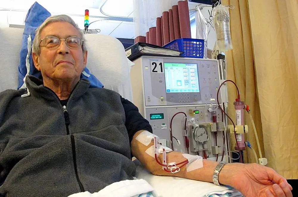 A man lying in a hospital bed, receiving haemodialysis. 