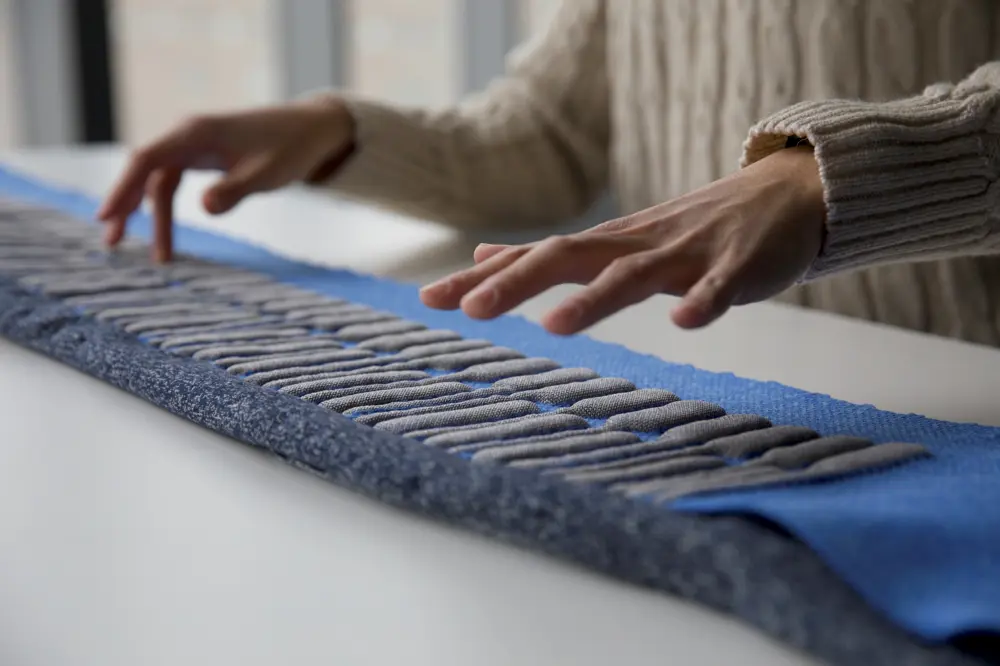 A pianist's hands are hovering over a blue and grey knitted keyboard, while triggering the theremin functionality of the device.