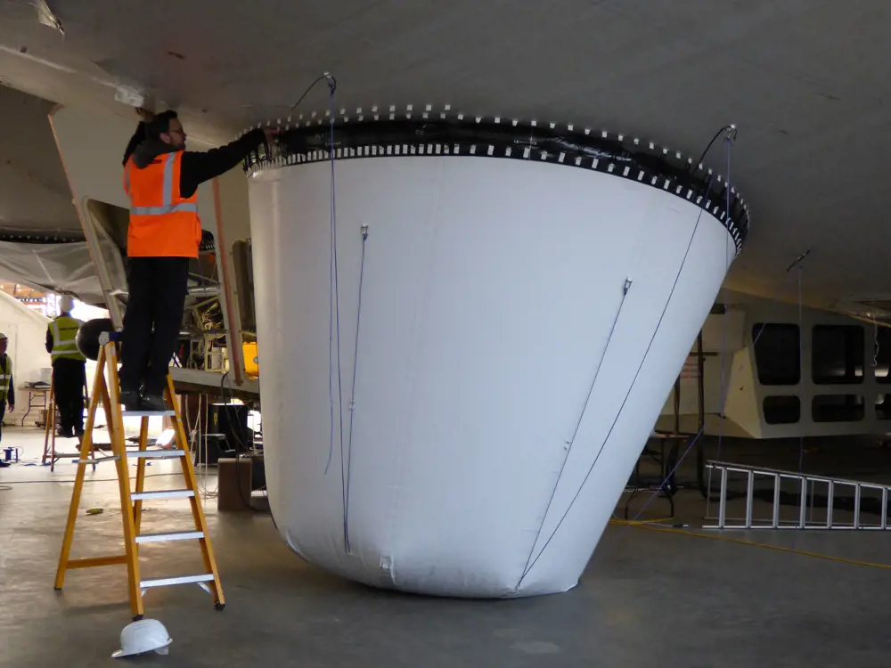 A person on a ladder working on a large airbag for the airbag underneath the Airlander. 