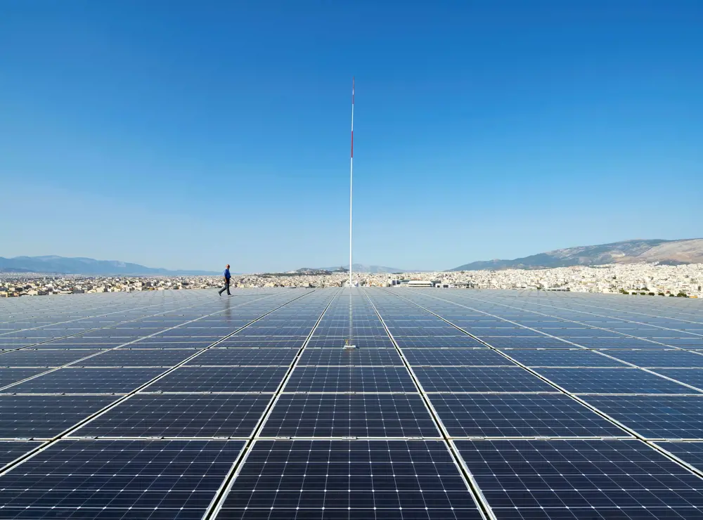 A person in the background walking among lots of solar panels. 