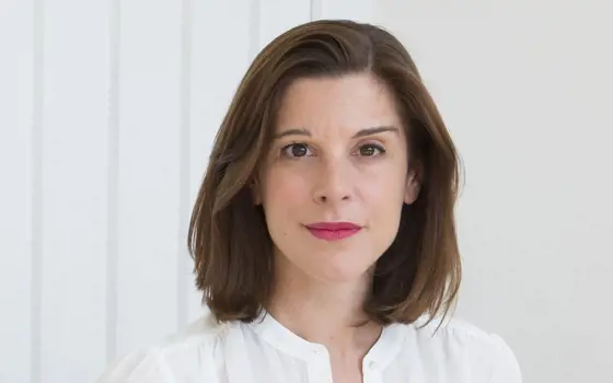 A woman wearing a white shirt, standing in front of a white wall.