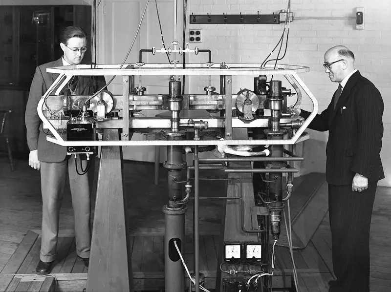 A greyscale image of two men standing next to the first accurate atomic clock.