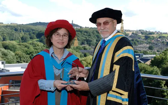 Professor Jiang and Sir Patrick Stewart in robes, holding a glass award.