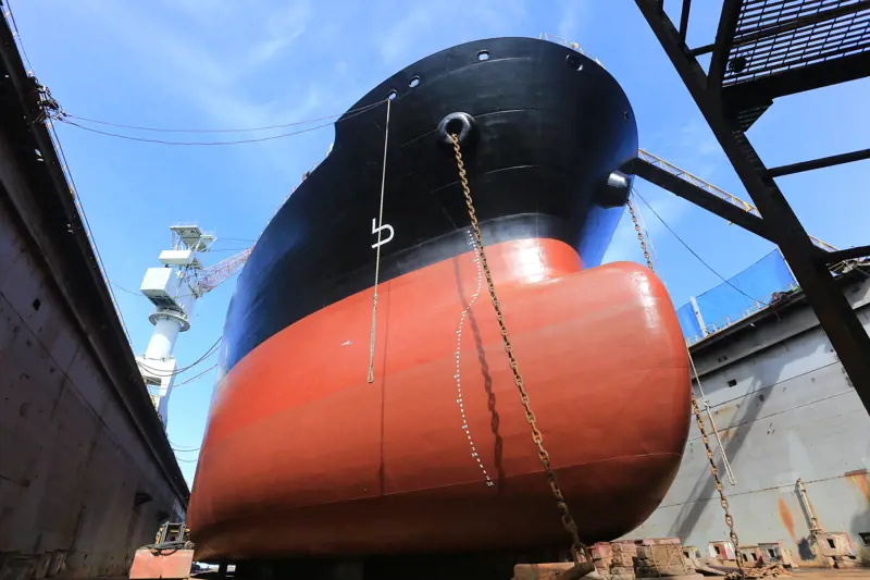 A ship's hull from below that is painted black at the top and red at the bottom. There are chains at each side of the hull