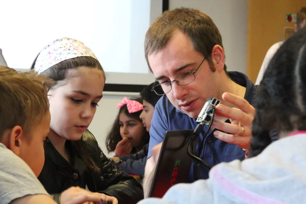 A teacher helping a child program a Raspberry Pi on a laptop.