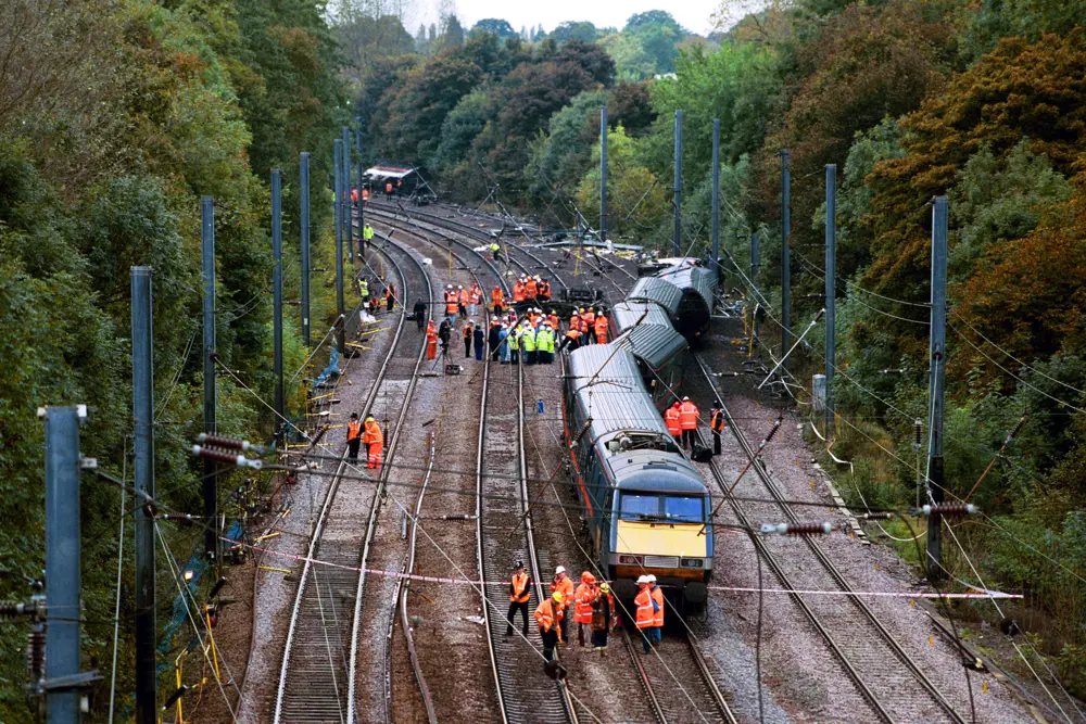 An aerial shot of a derailed train on tracks with workers in high visibility jackets gathered around it.