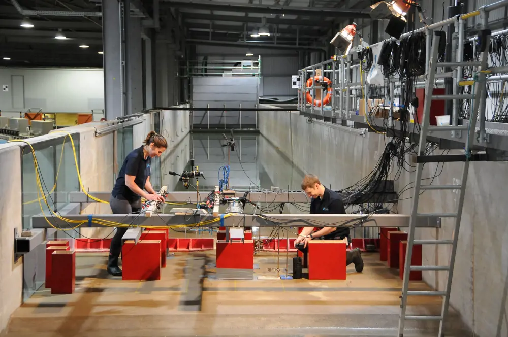 Two engineers setting up the model buildings connected to wires within the tsunami simulator at HR Wallingford.
