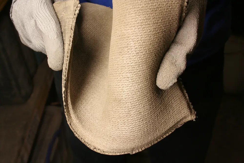 Close-up of a flexible sheet of Concrete Canvas held by gloved hands, showing the material's layered structure and fabric-like texture before hydration and setting.