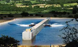 A large body of water outside with a wave generator and surfers.