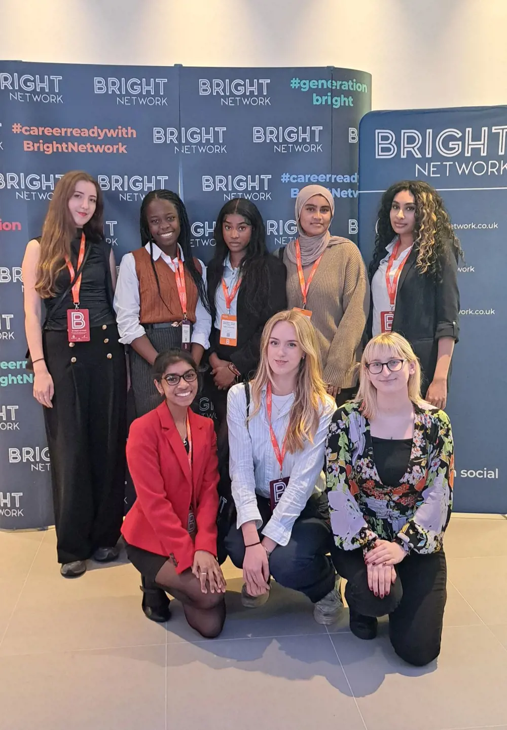 A group of eight women - three of whom are crouching down at the front - stand in front of a backdrop, looking at the camera
