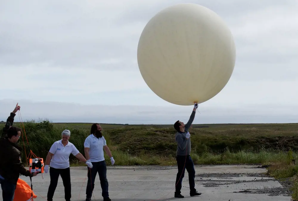 A person holding a large circular high-altitude floating balloon that is ready to be launched.