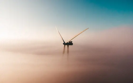 The top of a wind turbine peaking through orange mists in the sky.