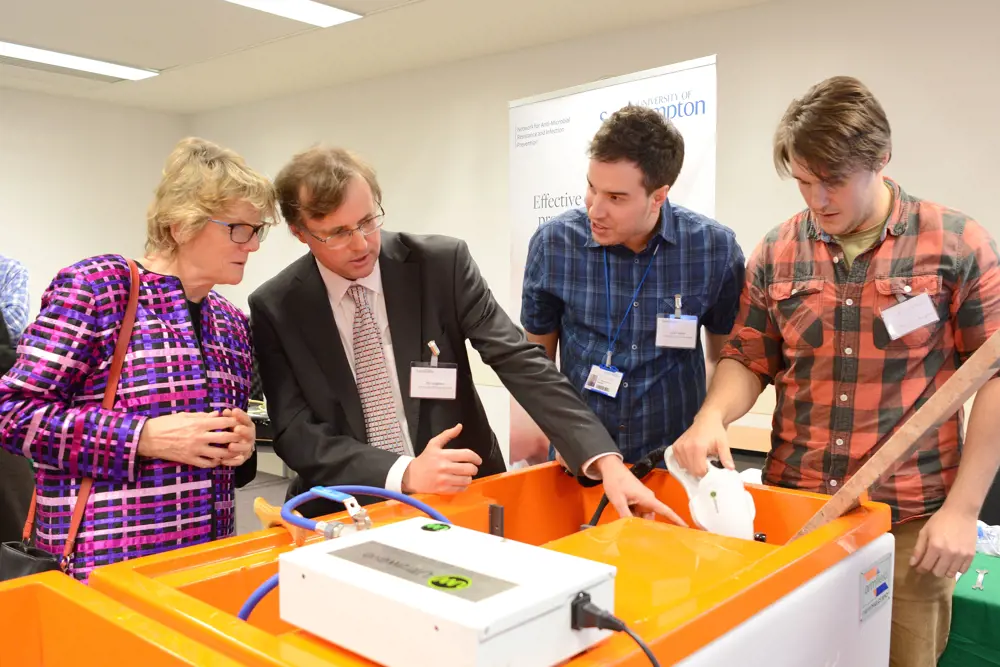 Professor Timothy Leighton standing next to Professor Dame Sally Davies behind a demonstration of the StarStream device, explaining how it works. 