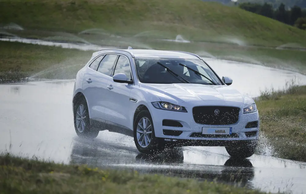 A white SUV vehicle drives round a bend in a road in wet conditions