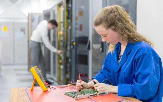 A young female engineering apprentice works on a circuit board.