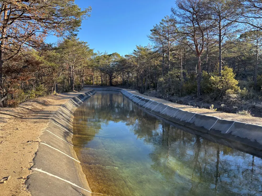 Concrete Canvas lining a water channel, with clear water flowing through a concrete-lined canal bordered by trees and vegetation.