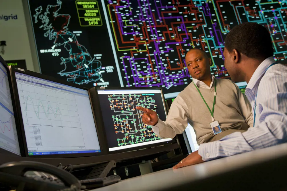 Two electrical engineers looking at a computer screen, with a map of the UK power network in the background.