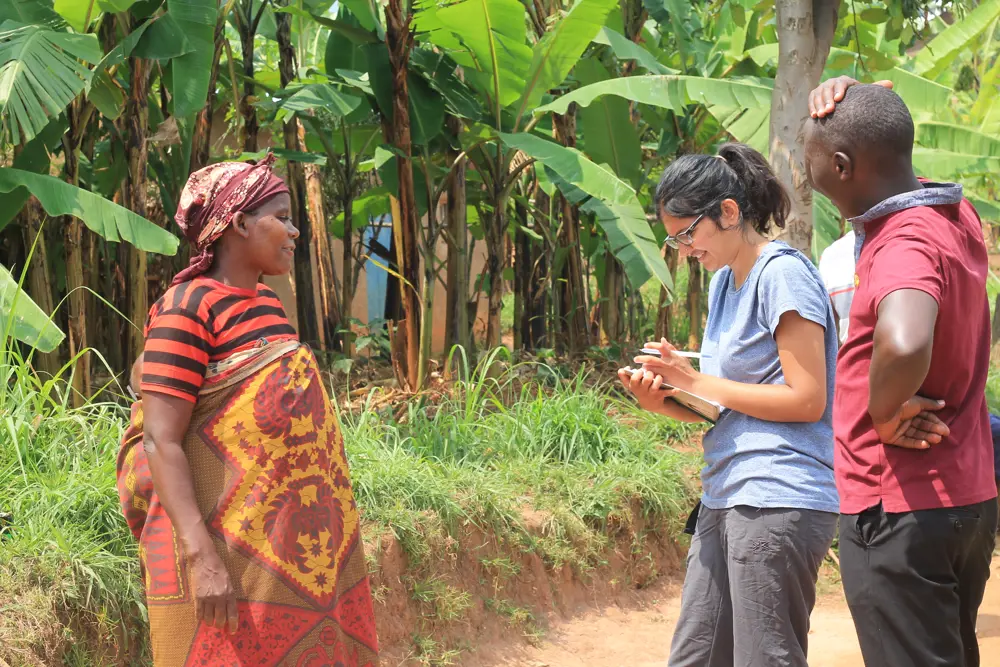 Aakeen Parikh writing in a notebook while talking to two local people in Minazi, Rwanda.