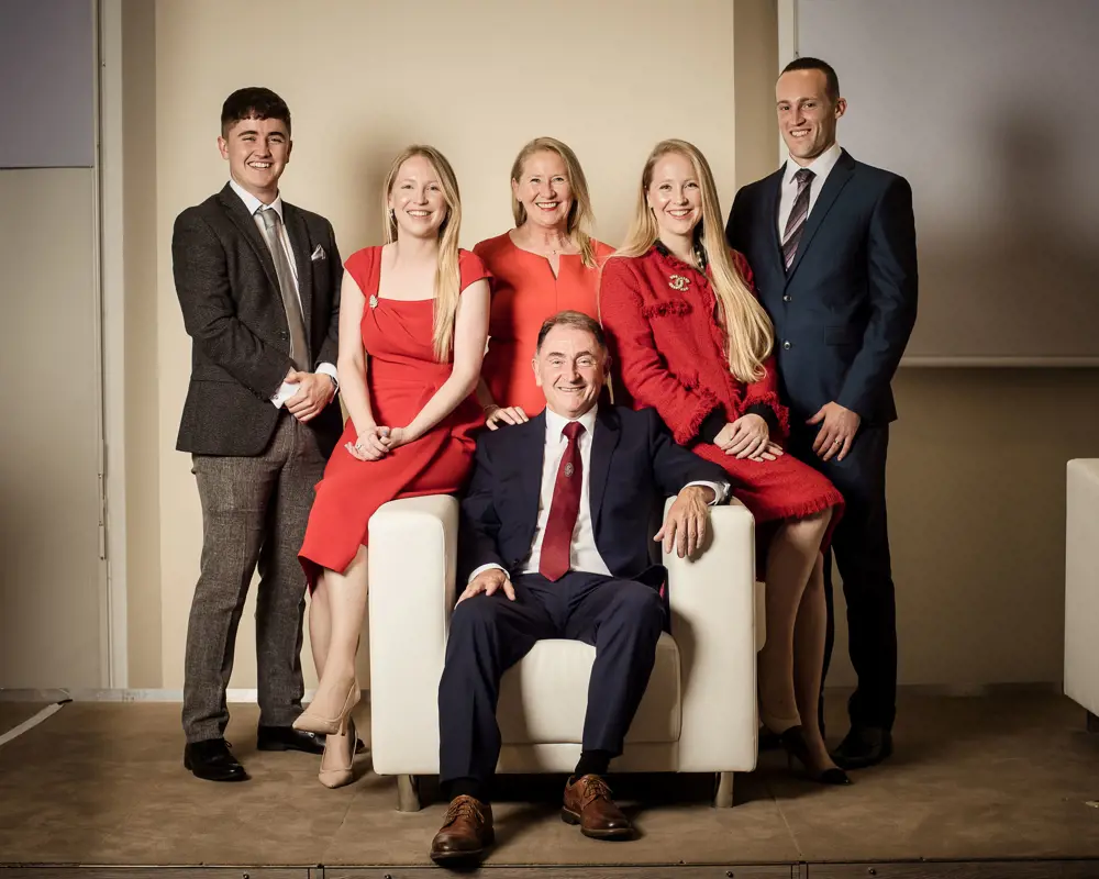 Sir Jim McDonald sitting down in a chair, surrounded by his family.