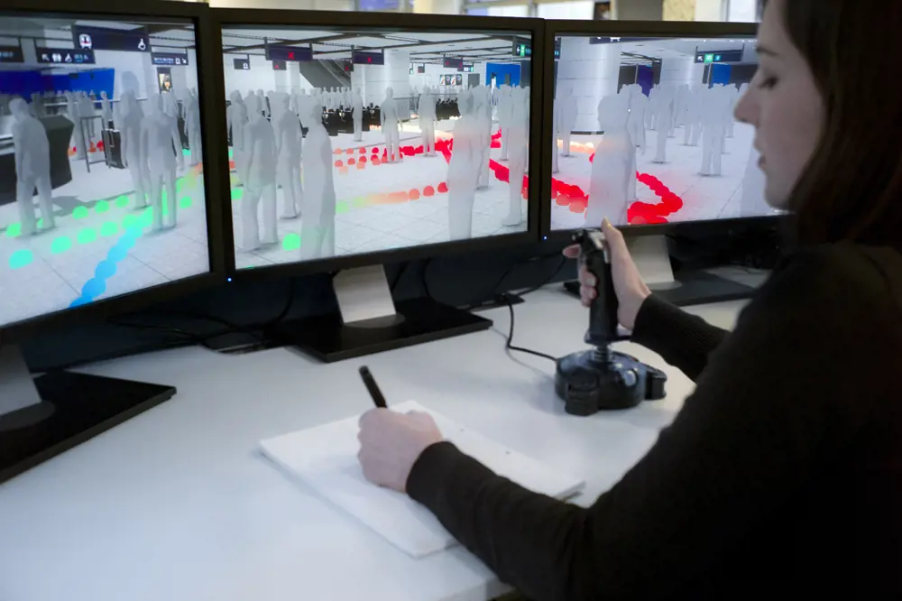 A female sitting at a desk in front of three screens, simulating people at an underground rail station. 