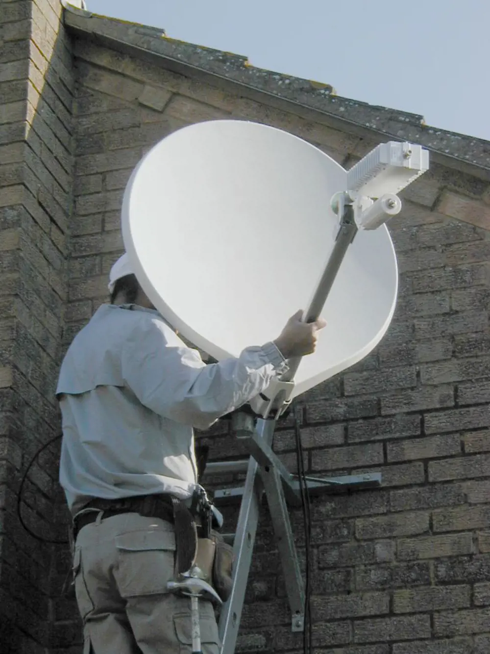 A worker on a ladder, holding a satellite dish.