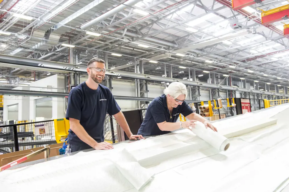 A man and a woman laughing in a factory as they handle the rolls of fibre used to make the composite material.