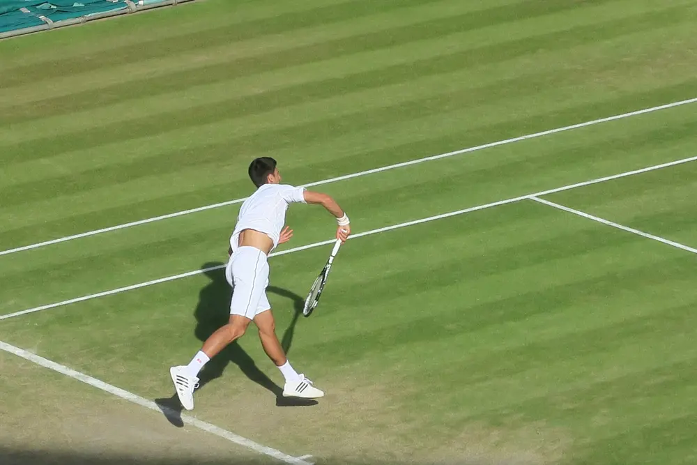 A man dressed in tennis whites and holding a tennis racket in motion on a grass tennis court