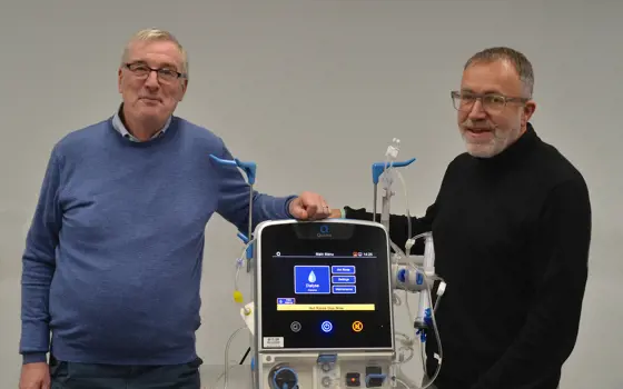 Two men stand either side of a dialysis machine