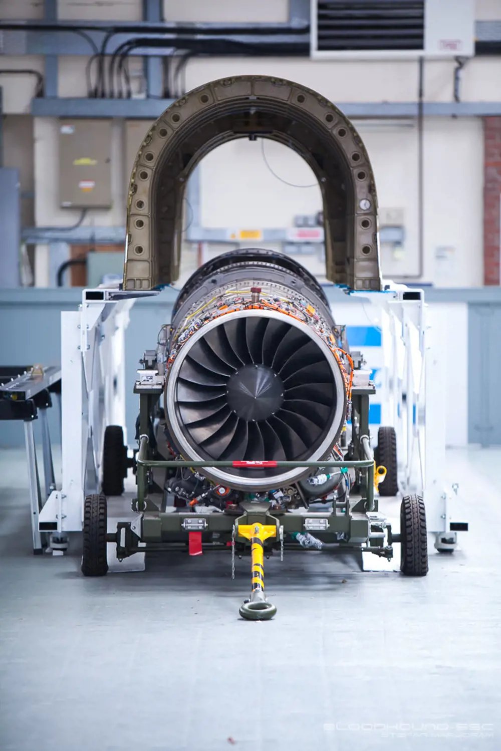 A jet engine on a stand with wheels in a factory.