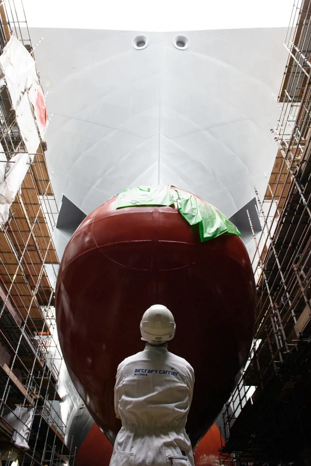 A person standing in a factory looking at the bow of the HMS Prince of Wales ship.